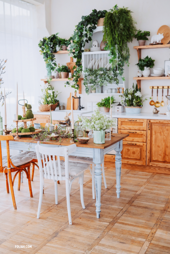 13 Gorgeous Kitchen Plant Styling Ideas You’ll Want to Copy 14 at Foliah Rustic kitchen with wooden shelves, cascading greenery, and a cozy dining table decorated with moss bunnies, delicate flowers, and vintage touches.