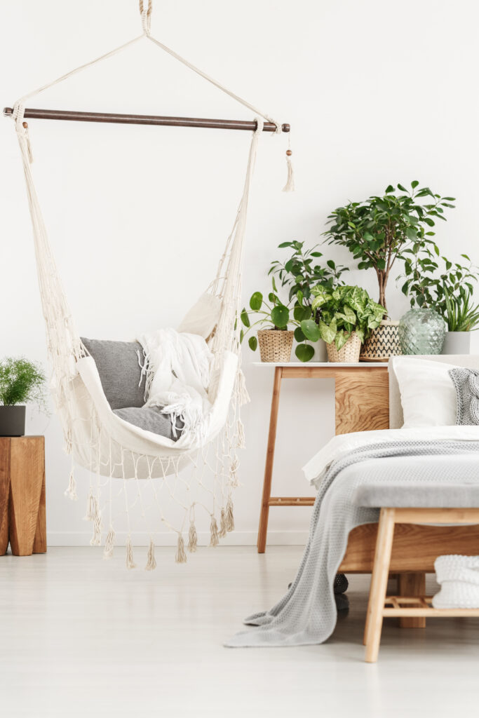 Bedroom corner with hanging chair and plants on a wooden table, creating a relaxed, cozy seating area with greenery.