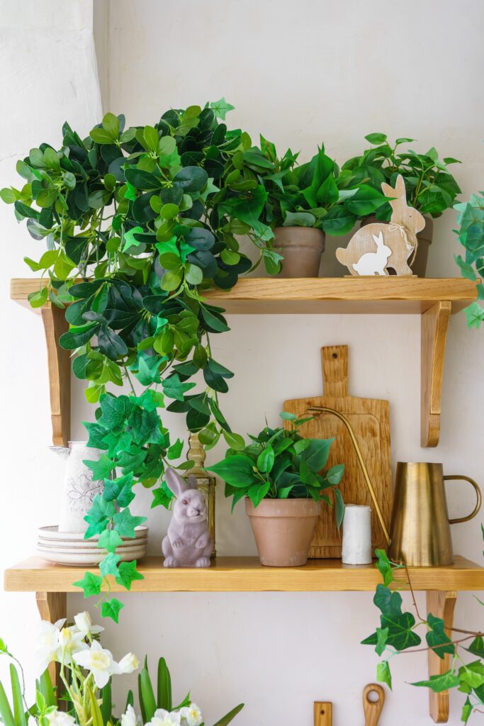 Wooden shelves styled with leafy plants, trailing greenery, and small bunny decor for natural Easter plant styling.