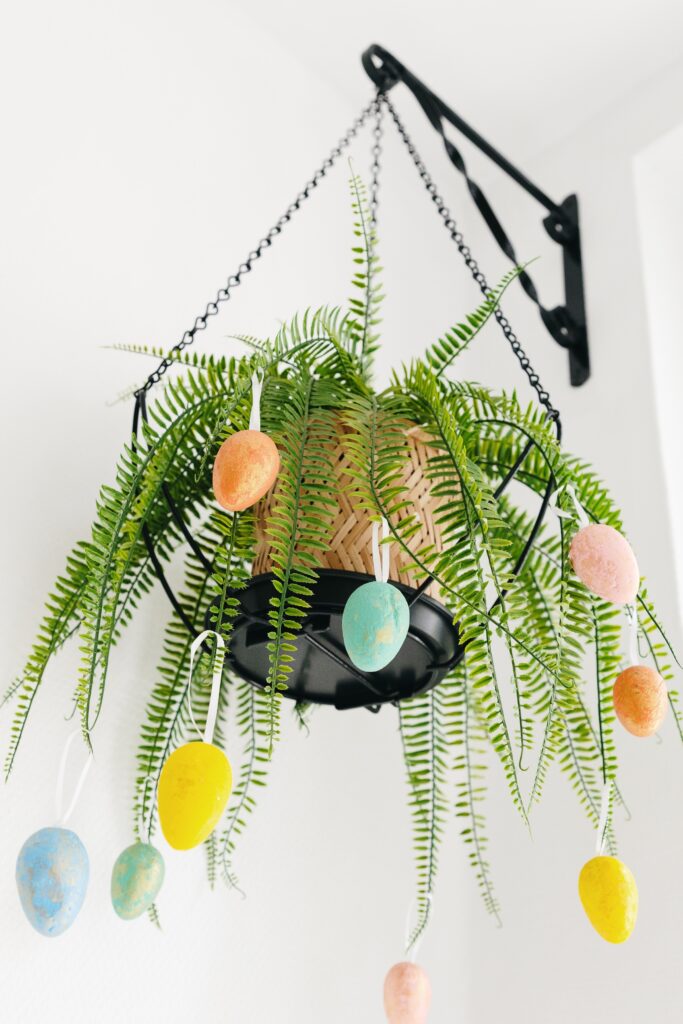 Hanging fern decorated with pastel Easter eggs for a simple and space-saving Easter plant display.