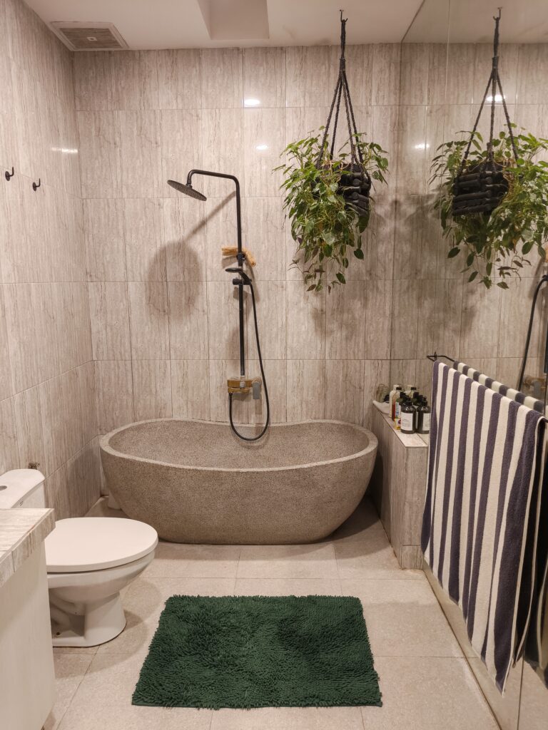 Modern minimalist bathroom interior with stone bathtub, walk in shower, marble wall tiles and natural decor. Clean luxury bathroom design with spa atmosphere and indoor plant.