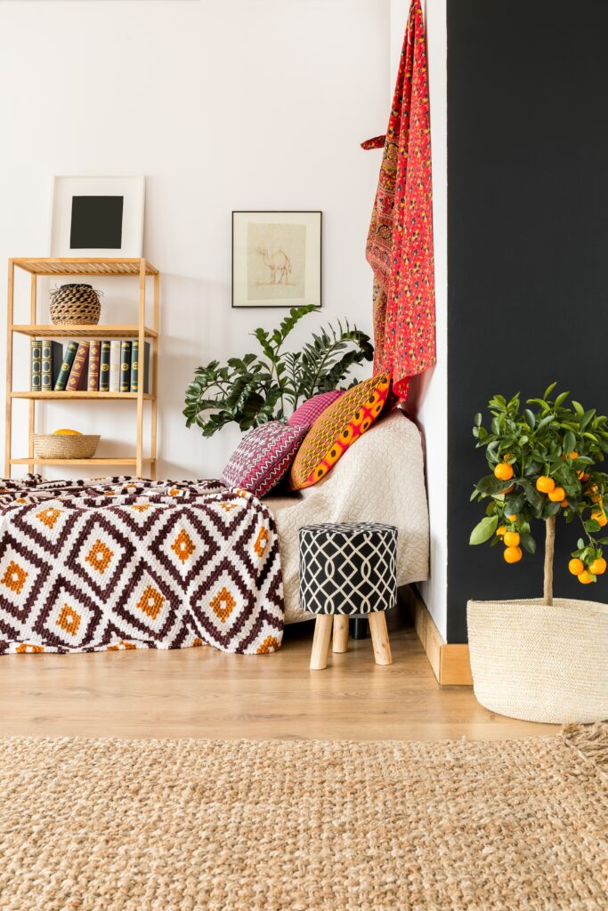 Bedroom corner with colorful textiles and a small potted citrus tree with orange fruit adding a bright focal point.