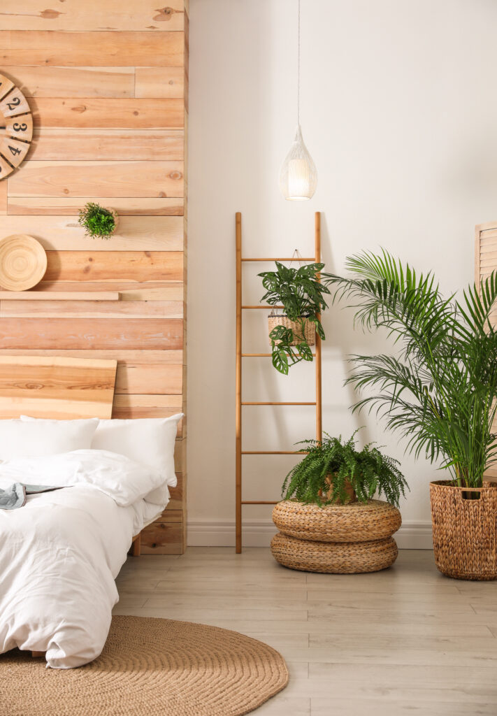 Bedroom corner with wooden ladder holding a hanging plant, with additional floor plants including a fern and palm in woven baskets.