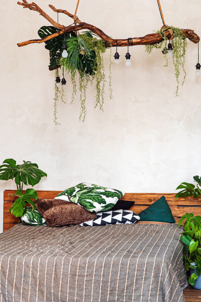 Bedroom with a wooden branch suspended above the bed, holding hanging plants and string lights for a natural, relaxed look.