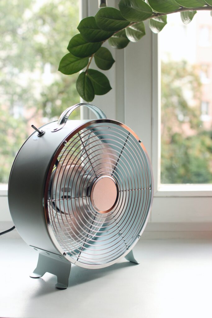 metallic fan cooling a room in summer heat with house plant frond